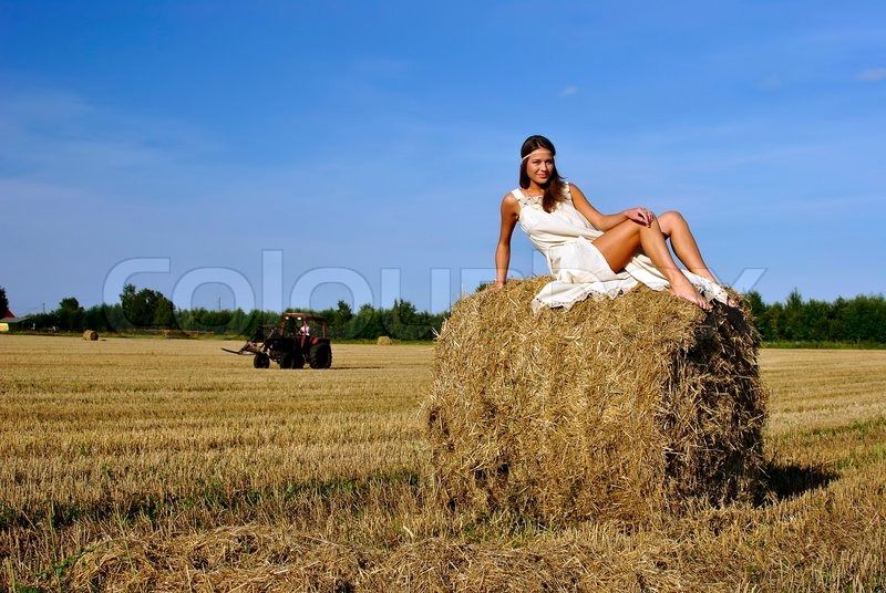 Girl in a rural clothing standing on the field, tractor on the