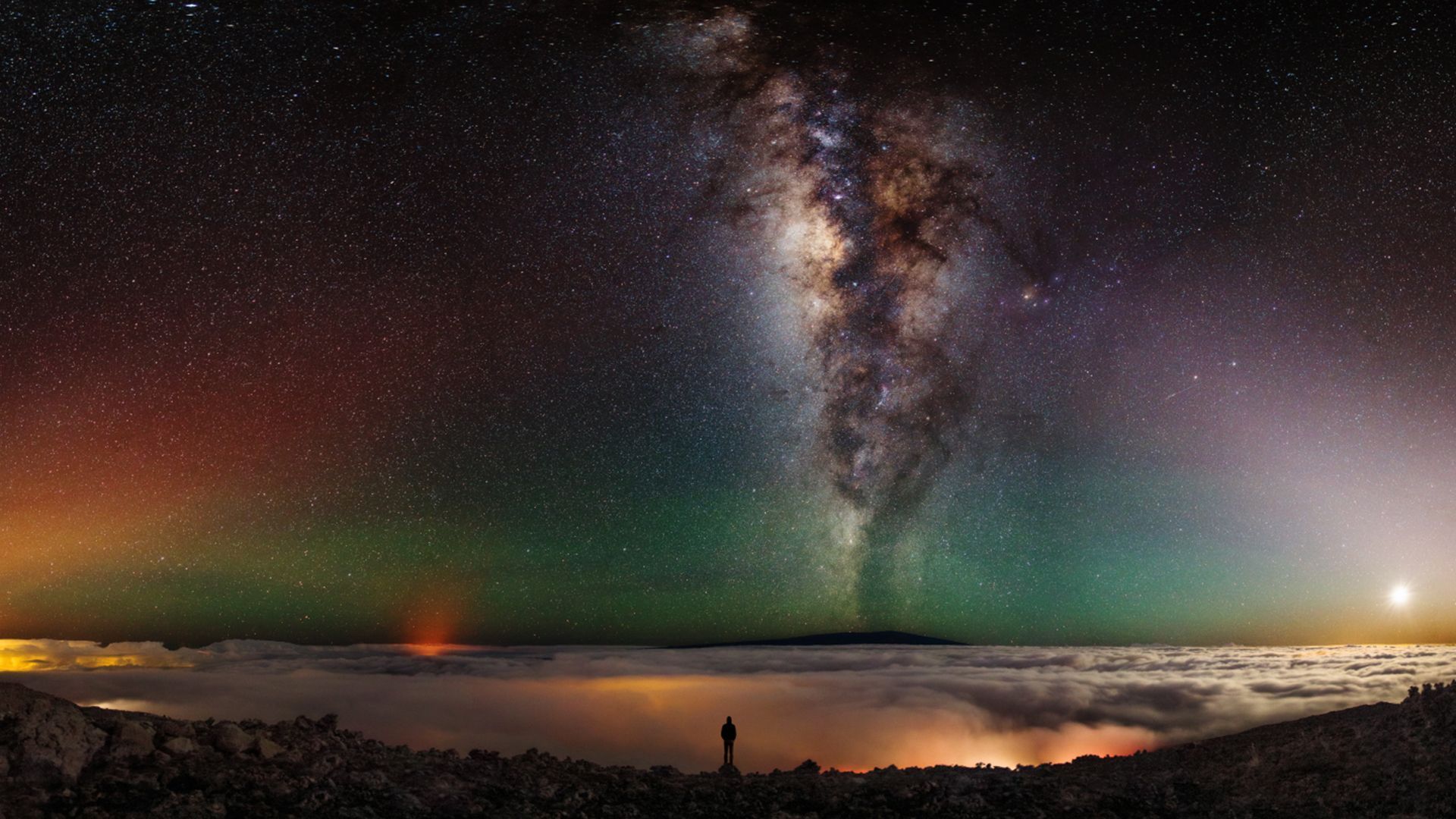 Man standing at edge of volcano with milky way, planets in